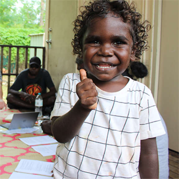 A smiling Indigenous child gives a 'thumbs up'