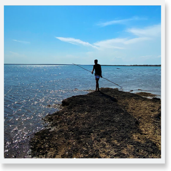 Silhouette of an Indigenous man with a spear where an outcrop of land meets the ocean