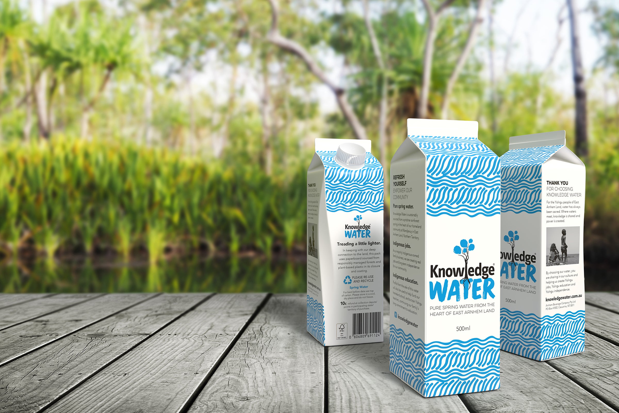 Three cartons of Knowledge Water on a timber deck in front of a rainforest spring at the Manjawuy Indigenous Community